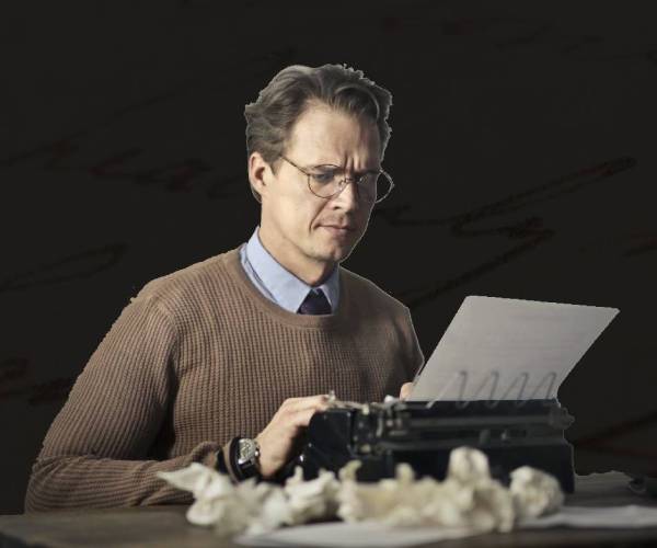 A man sitting at a table with papers and typewriter.